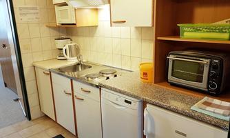 A small, modern kitchen with white cabinets and a countertop. It is equipped with a sink, a stove, a microwave, and a dishwasher.