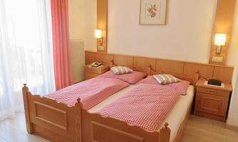 A cozy bedroom with two single beds in a wood look. The walls are light, and there is soft light from the lamps.