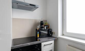 A modern kitchen with a cooktop, a range hood, and a microwave. Next to the window are some kitchen utensils and bottles of oil.