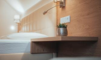 A modern bedroom with a cozy bed and a wooden table. On the table is a small plant, and there are wall lamps.