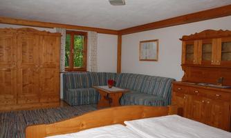 A cozy room with wooden cabinets and a striped couch. A table with a flower vase and a large bed complete the ambiance.