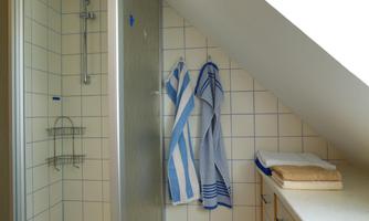 A modern bathroom with a shower and white tiles. Hair towels in blue and white hang on the wall.