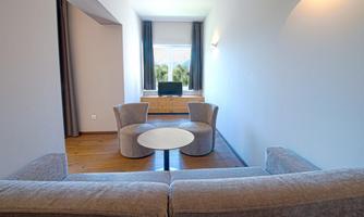 A modern living room with a gray sofa and two small armchairs. There is a round table and a television in the corner.