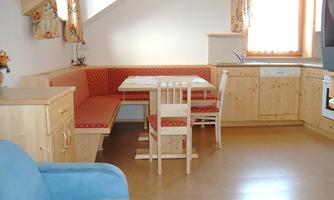 A bright kitchen with wooden furniture and a cozy dining area. There is a small table with chairs and a sofa in the corner.