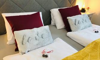A cozy bedroom with two single beds. The pillows are adorned with the word "love" and there is a yellow blanket as well as decorative elements.