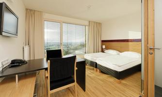 A modern hotel room with two beds and a desk.  
Large windows let in plenty of light and provide a view outside.