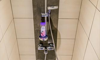 A modern shower with a simple faucet on a tiled wall. Under the faucet is a bottle of shower gel.