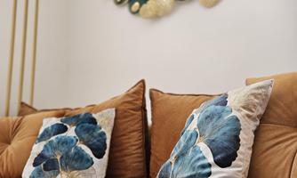 A cozy sofa with a brown cover and cushions in shades of blue and green. Decorative elements hang on the wall, adding a modern touch.