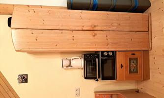 A small kitchen corner with a wooden cabinet, a microwave, and a coffee machine. Next to the cabinet are several blue containers.