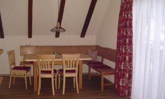 A cozy dining area with a wooden table and chairs. The windows are adorned with curtains featuring a floral pattern.