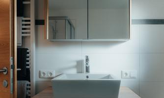 A modern bathroom with a white sink on a wooden cabinet. A large mirror cabinet is hanging on the wall.