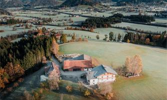 A picturesque landscape with a large meadow and tall trees. In the foreground, there is a charming country house.