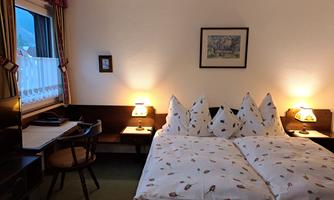 A cozy bedroom with a double bed and lovingly folded pillows. The room features a desk and warm light from the bedside lamps.