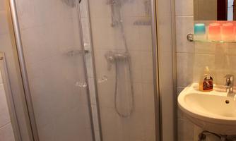 A small bathroom with a shower cabin and a sink. The walls are tiled in light colors and the floor is covered with tiles.