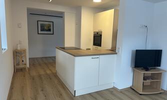 A modern kitchen with a cooking island and light furniture. The room has a friendly atmosphere with a wooden floor and plenty of light.