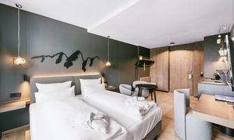 A modern hotel room with two single beds and stylish furniture. The walls are painted in neutral tones and there is a cozy seating area.