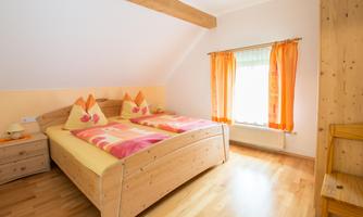 A simple bedroom with a double bed and wooden furniture. The windows have orange curtains that let in a lot of light.