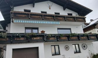 A traditional house with wooden balconies and a modern garage door. The façade is painted light and has decorative elements.