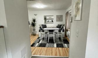 A bright hallway leads into a modern living area. The room is cozy and furnished with a table and chairs as well as a seating group.