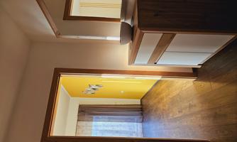 A bright hallway with a wooden cabinet and a mirror. In the background, there is a yellow room with curtains.