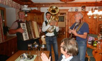 A cozy Alpine cabin with three musicians playing traditionally. In the foreground, guests are sitting and enjoying the music and the ambiance.