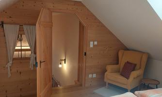 A cozy bedroom with wooden walls and a window in the roof. A comfortable armchair is next to the bed.