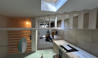 A modern kitchen with wooden shelves and a wooden staircase. In the background, a cozy living area can be seen.