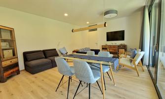 A modern living room with a dining table and elegant chairs. The decor is bright and inviting, with a cozy sofa and large windows.