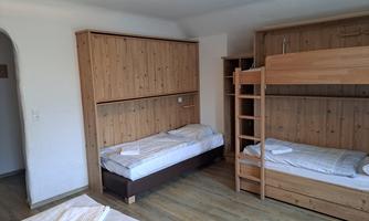 A simple room with wooden shelves and two bunk beds. The beds are unmade and the floor is made of wood.
