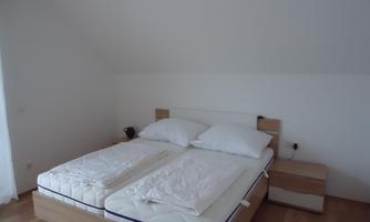 A cozy bedroom with a double bed and two mattresses. The walls are light and the floor is made of wood.