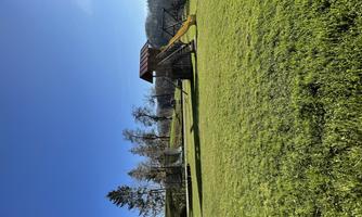 A playground with a slide and swings on a green meadow. The sky is clear and blue.