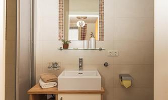 A modern bathroom with a sink and a large mirror. There are wooden shelves and some decorative elements.