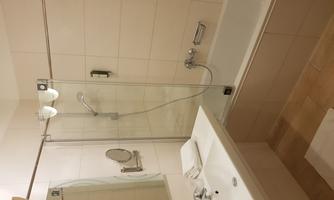 A modern bathroom with a bathtub and a glass shower partition. Fresh towels are on the sink and a large mirror is present.