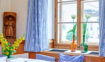 A cozy dining area with a wooden balcony and blue curtains. Fresh flowers and decorative bottles are displayed on the table.