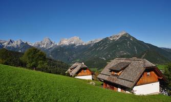 A picturesque Alpine landscape with two charming cottages on a green meadow. In the background, majestic mountains rise under a clear blue sky.