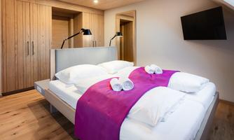 A modern bedroom with a double bed and fresh white bed sheets. The wood paneling and soft lighting create an inviting atmosphere.