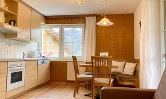 A cozy kitchen with wooden details and a dining area. The large window provides plenty of daylight.