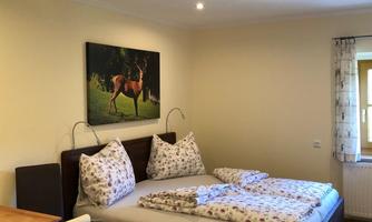 A cozy bedroom with a double bed and floral bedding. On the wall hangs a picture of a deer, and there is a small table with chairs.