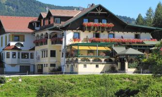 A charming hotel with blooming balcony plants and traditional architecture. Surrounded by green meadows and mountains in the background.