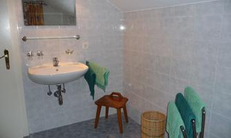 A simple bathroom with a sink and a mirror. Towels in various colors and a wooden chair are also visible.