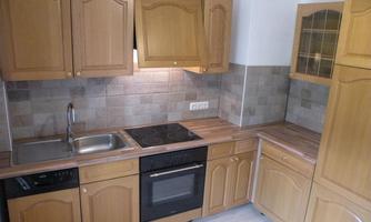 A modern kitchen with wooden cabinets and a practical workspace. It is equipped with a stove, oven, and sink.