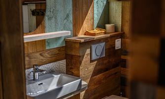 A modern bathroom with wood-clad walls and an elegant sink. On the shelf, there are towels and a decorative vase.