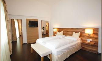 An elegant bedroom with a large bed and comfortable bedding. The walls are painted in light colors and there is a television as well as refurbished wooden furniture.