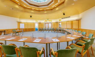 A modern conference room with a round table arrangement and chairs. Light filters through a large skylight, creating a pleasant atmosphere.