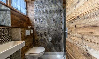A modern bathroom with wooden paneling and stylish tiles. The shower is separated by a clear glass wall.