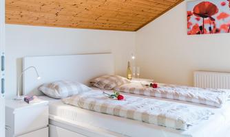 A cozy bedroom with two beds and a wooden ceiling. On the beds are cushions and fresh roses, and on the wall hangs a picture frame with a Poppies illustration.