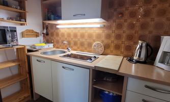 A cozy kitchen with a modern sink and stove. The walls are decorated with a brown tile pattern.
