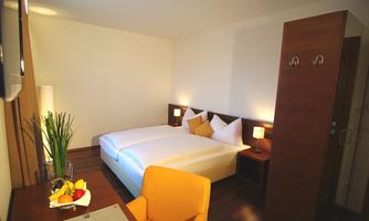 A bright hotel room with a double bed and modern furniture. There is a small table with fruit and a comfortable chair.