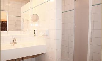 A modern bathroom with white tiles and a large sink. The shower is separate and there is a large mirror.