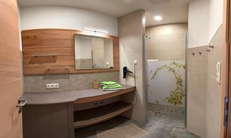 A modern bathroom with wood and stone accents. It features a mirror, a shower, and towels on a shelf.